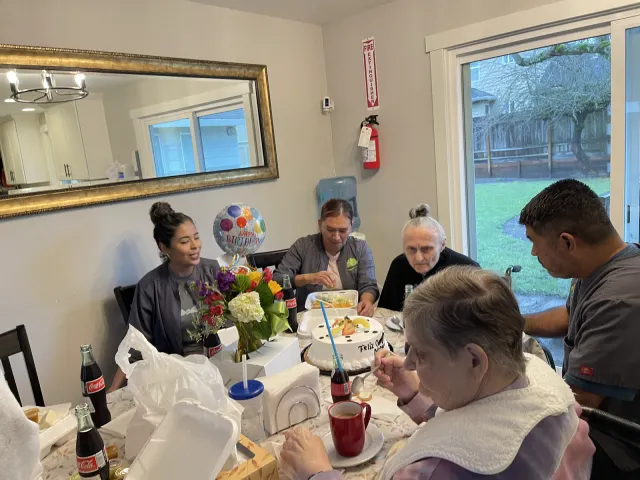 Residents and caregivers gathered around the dining table for a birthday cake.