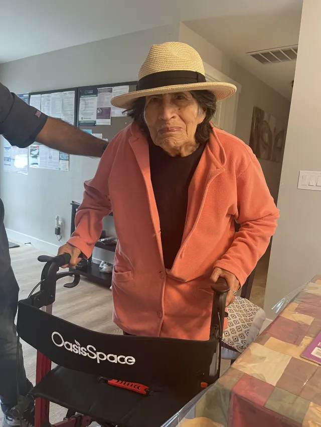A resident in a sun hat standing with her walker in the hallway.