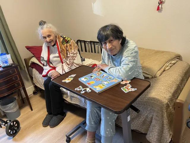Two residents working on a wooden puzzle together in a bedroom.